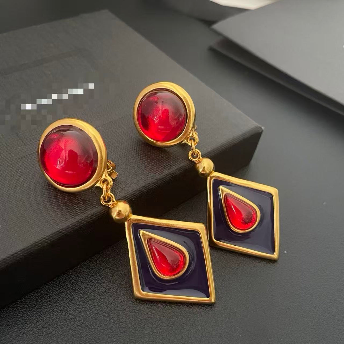 Clip-on earrings with glossy red resin tops, dark diamond-shaped enamel drops, red teardrop accents and gold-tone frames