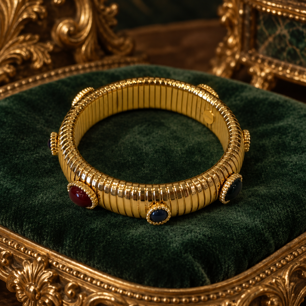 One gold-tone ribbed bangle with red and dark blue oval accents on green velvet