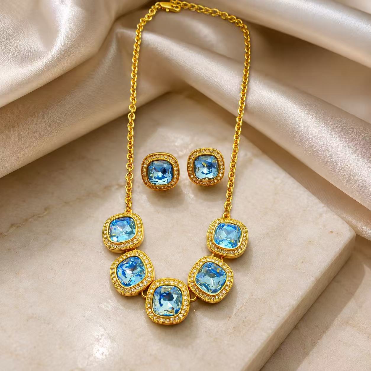 Light blue rhinestone necklace and matching stud earrings set on champagne fabric