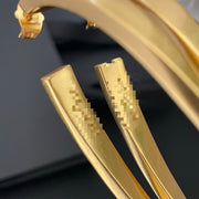 Detail view of the curved gold-tone finish on sculptural long stud earrings