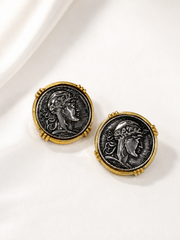 Pair of gold-tone coin-inspired portrait stud earrings with dark silver-tone centers on white satin