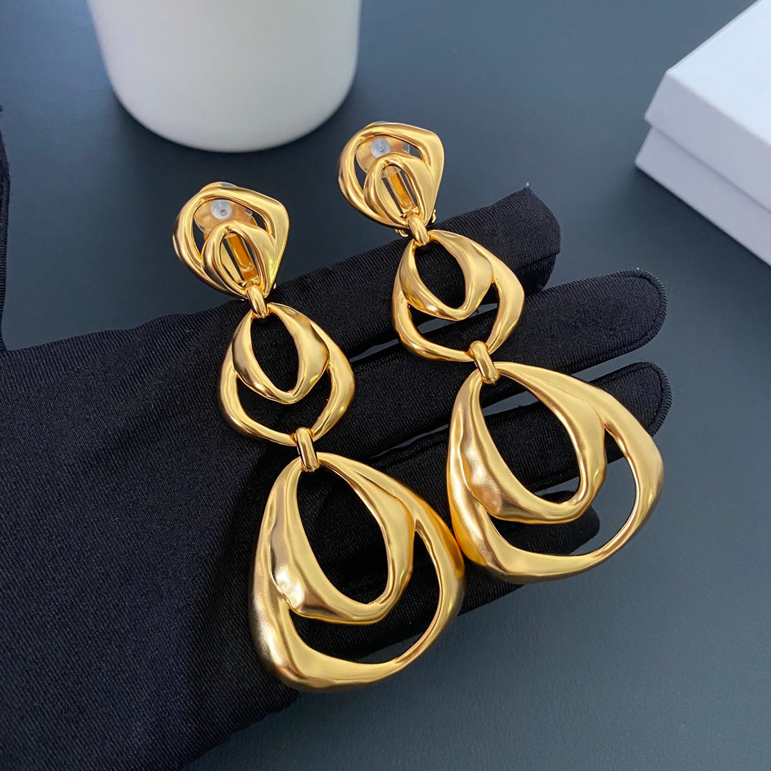 24K gold-tone organic drop clip-on earrings held on a black glove