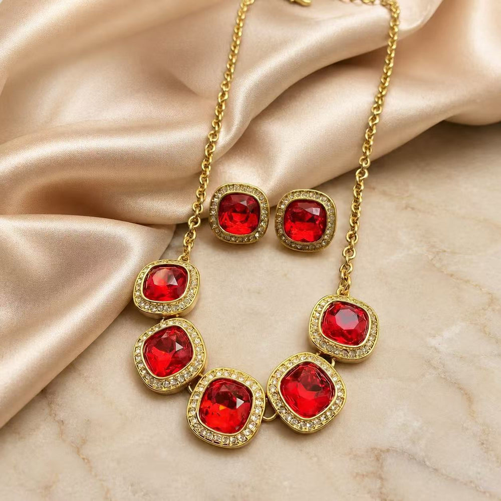 Red rhinestone necklace and matching stud earrings set on champagne fabric