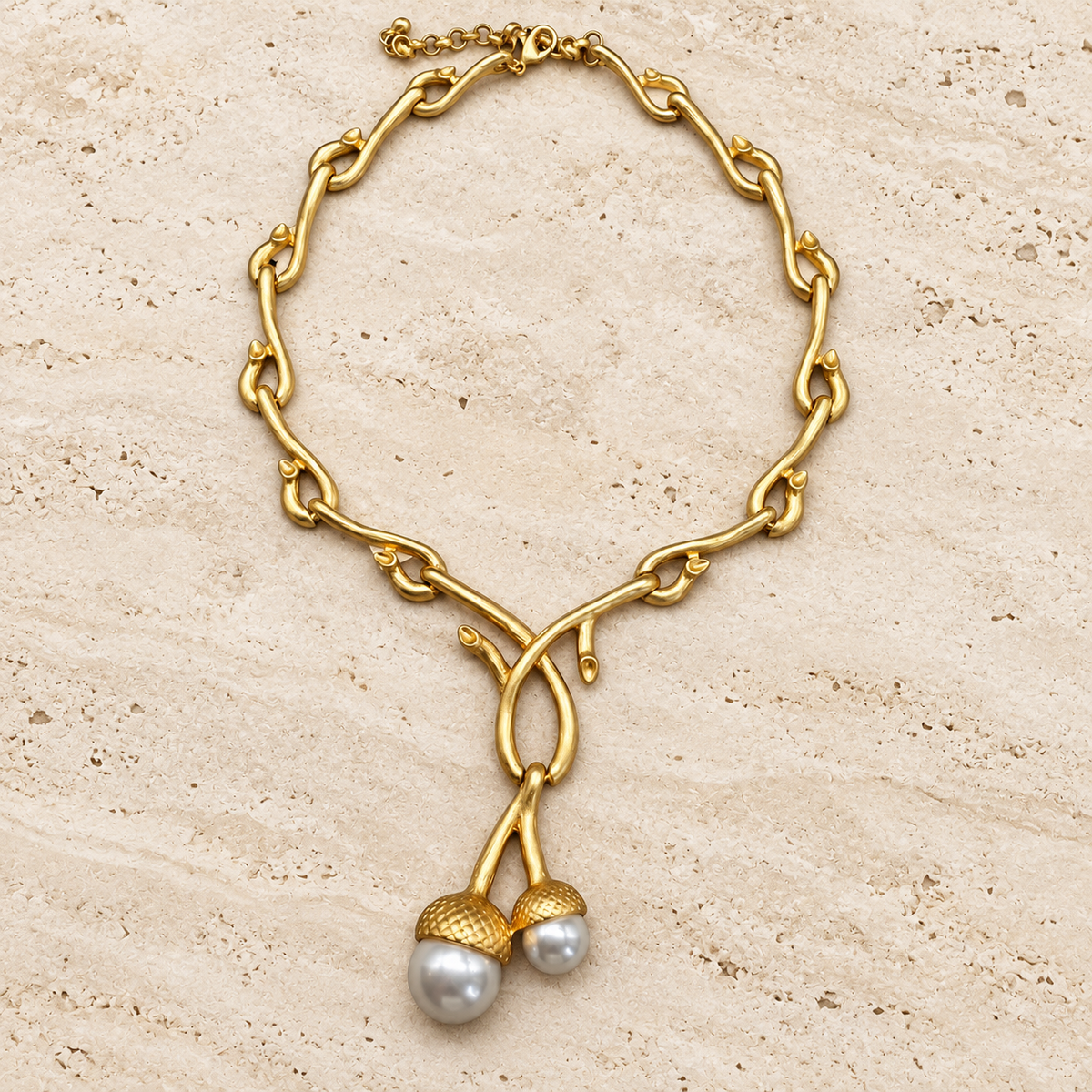 Gold-tone sculptural bamboo-link necklace with two rounded pearl-style drops beneath textured caps