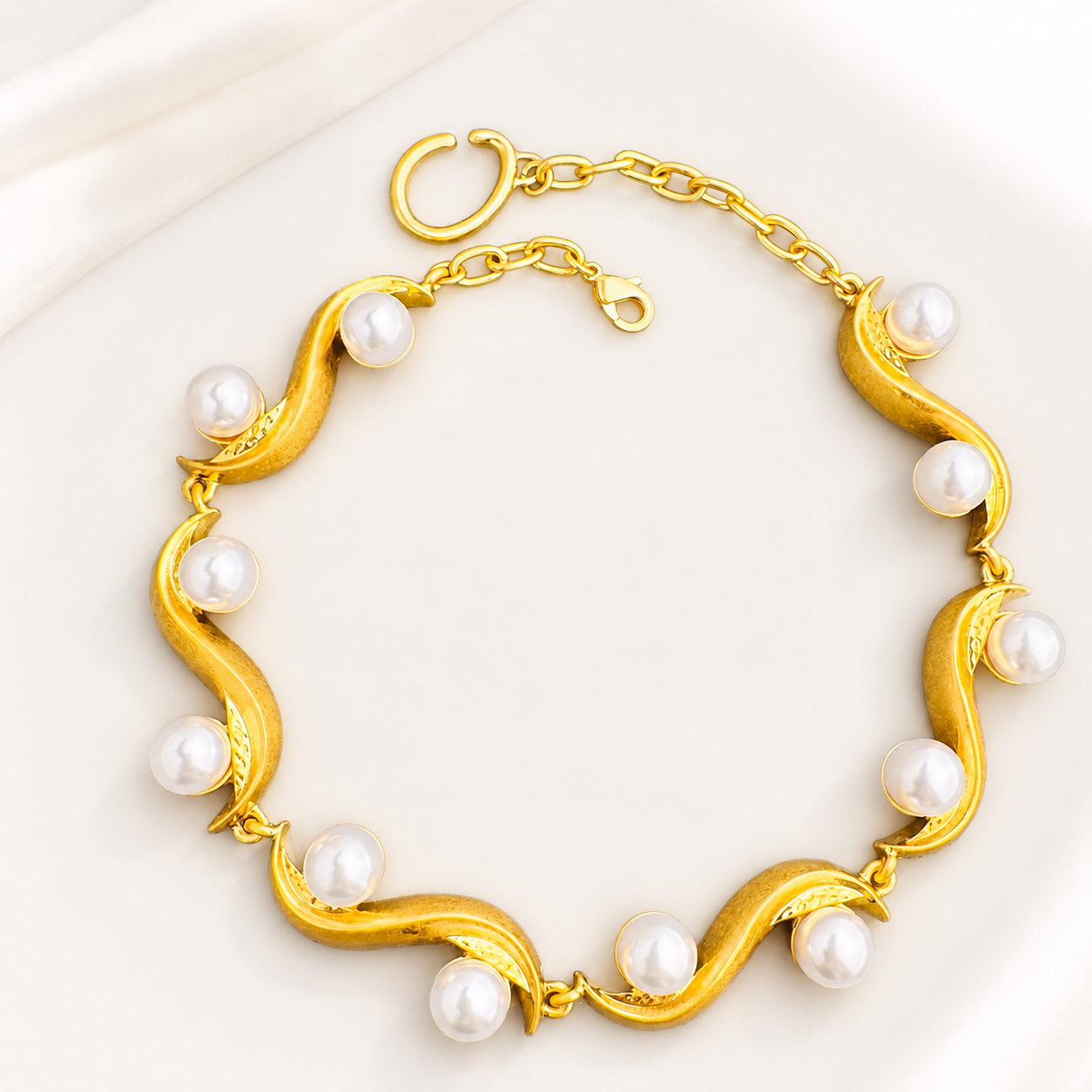 Gold-tone sculptural wave bracelet with white pearl-style accents