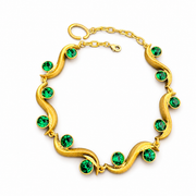 Gold-tone sculptural wave bracelet with peacock green faceted crystal-style accents