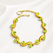 Gold-tone sculptural wave bracelet with light green faceted crystal-style accents