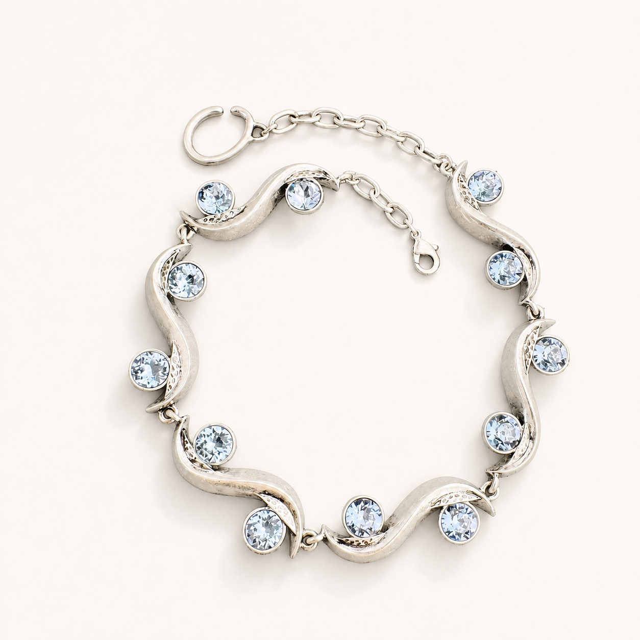 Silver-tone sculptural wave bracelet with light blue faceted crystal-style accents