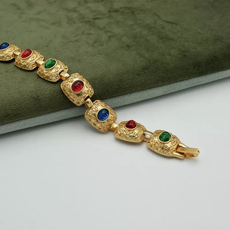 Close-up of ornate gold-tone bracelet links with red, green and blue oval accents on a green display