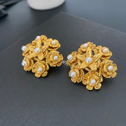 Angled view of floral pearl clip-on earrings showing layered gold flowers and white pearl accents.