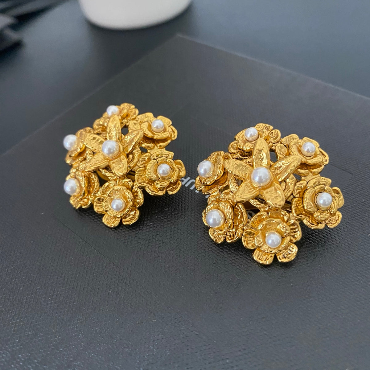 Angled view of floral pearl clip-on earrings showing layered gold flowers and white pearl accents.