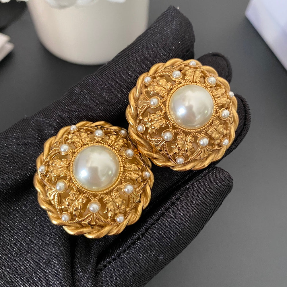 Close front view of French-inspired gold-tone medallion clip-on earrings with pearl-style accents