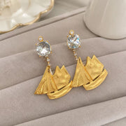 Front view of 18K gold-plated sailboat drop clip-on earrings on a light display surface