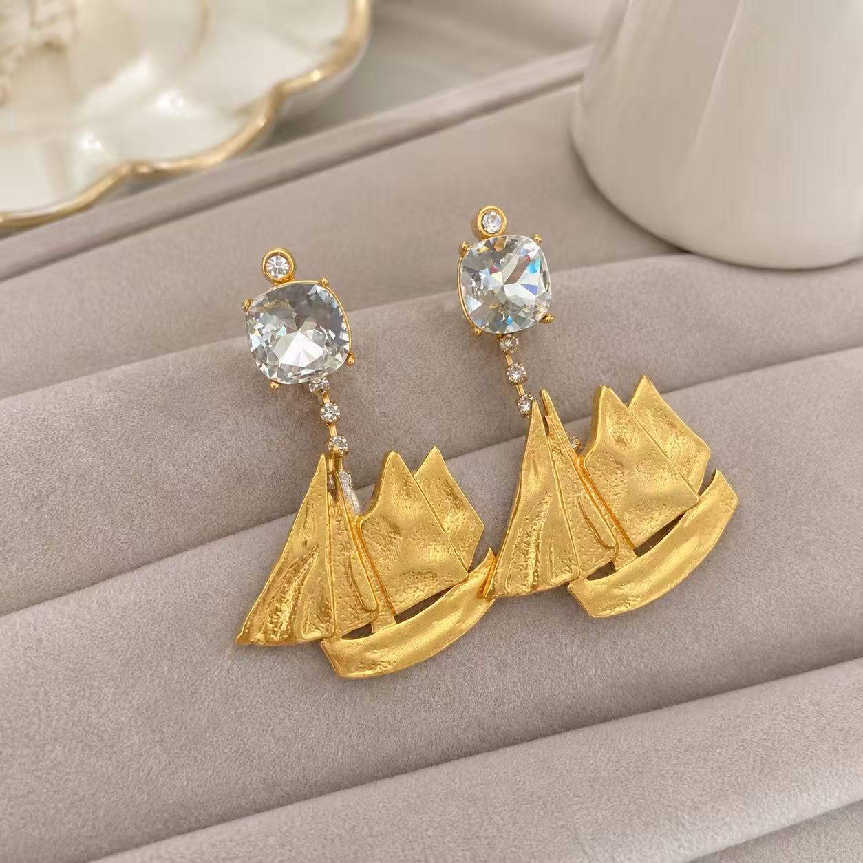 Front view of 18K gold-plated sailboat drop clip-on earrings on a light display surface