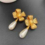 Front view of French-inspired 18K gold-plated bow clip-on earrings with pearl-style teardrop pendants