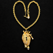 Gold-tone anatomical heart pendant necklace with keyhole cutout, clear sparkling accents and dangling charms