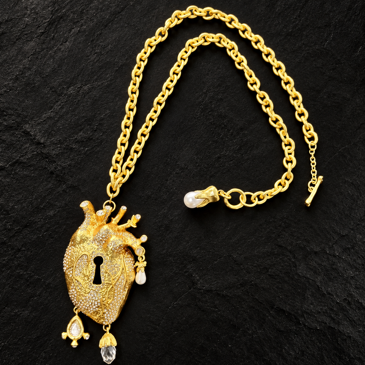 Angled view of sculptural heart keyhole pendant with clear accents, pearl-style drops and oval-link chain