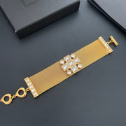 Gold-tone mesh bracelet laid flat with a geometric clear square-stone centrepiece