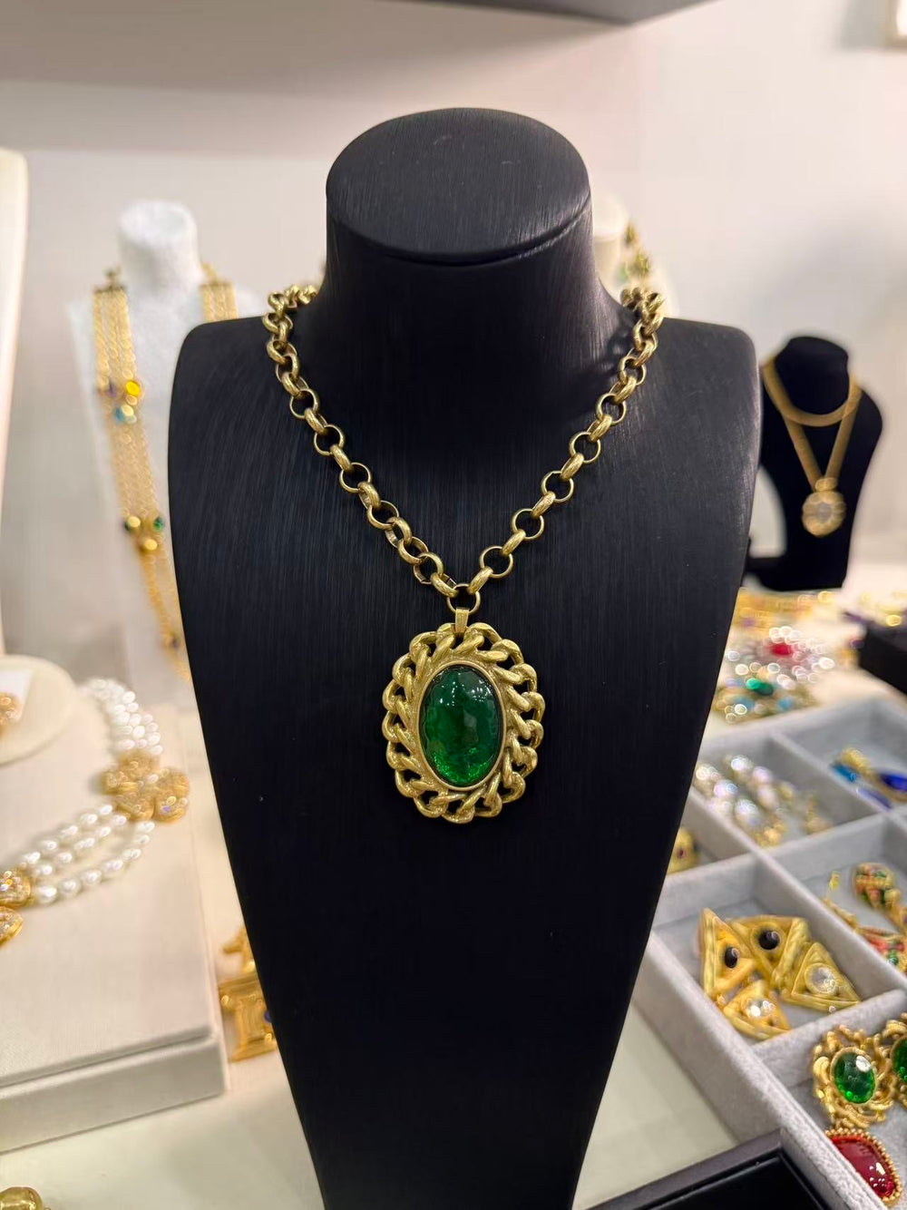 Gold-tone round-link necklace with a green oval pendant and interlocking-link frame on a black display bust