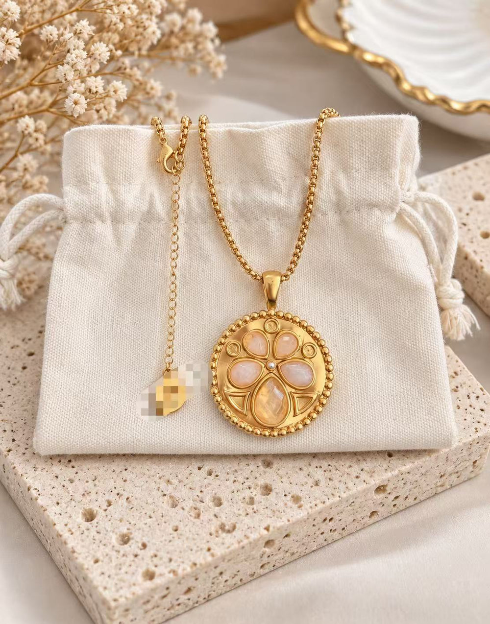24K gold-plated medallion pendant necklace with peach-pink teardrop accents and a beaded border displayed on a cream pouch