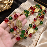 Close-up of the red and green glass beads, gold-tone chain links and ornate oval medallions of the long necklace