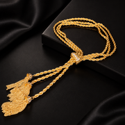Gold-tone triple rope chain tassel necklace laid flat on a black display box, showing the decorative centre band and tassel details