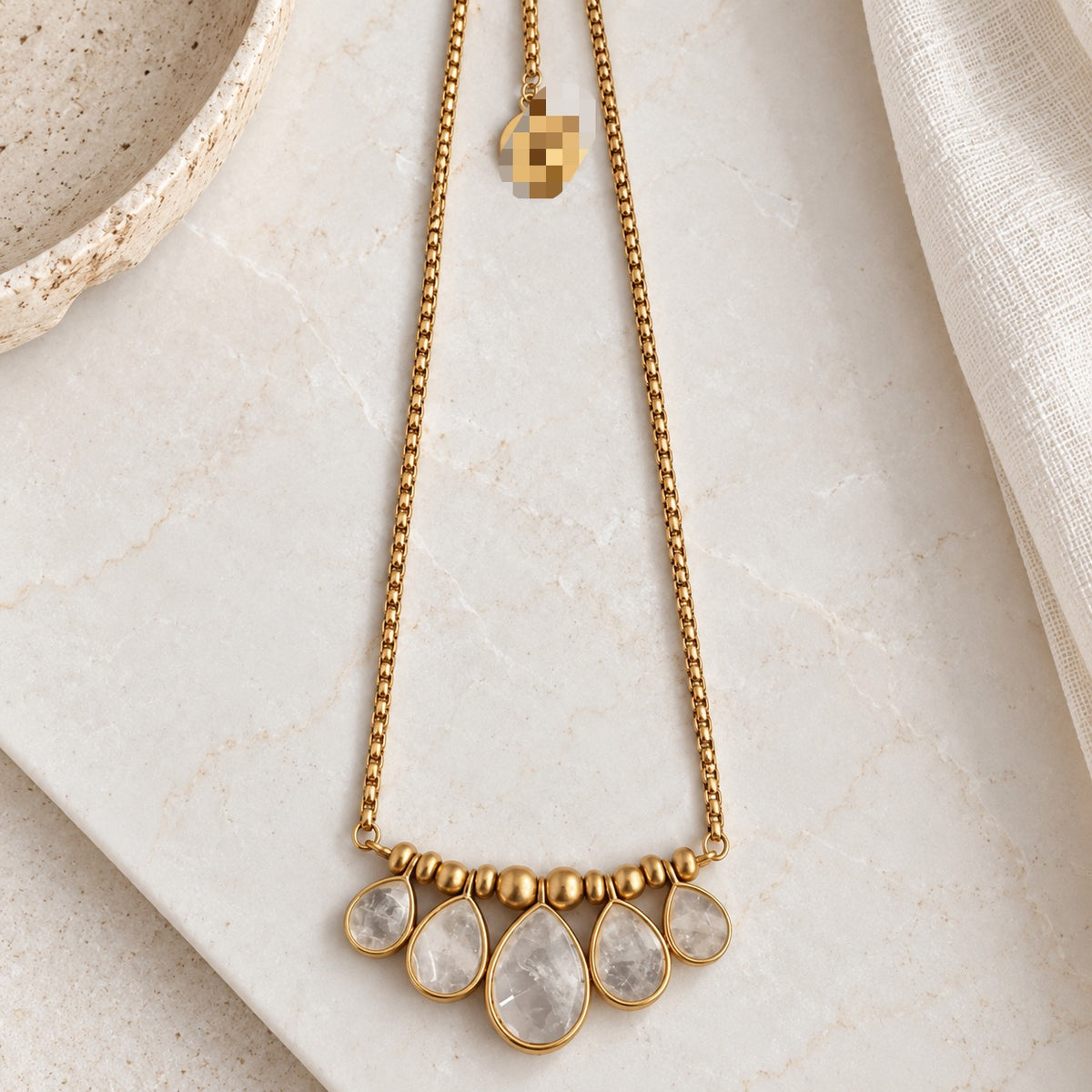 Front view of the five graduated teardrop crystal pendants and gold-plated chain on a light stone surface