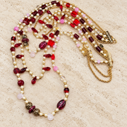 Red crystal and pearl-style multi-strand necklace with gold-tone chains laid flat