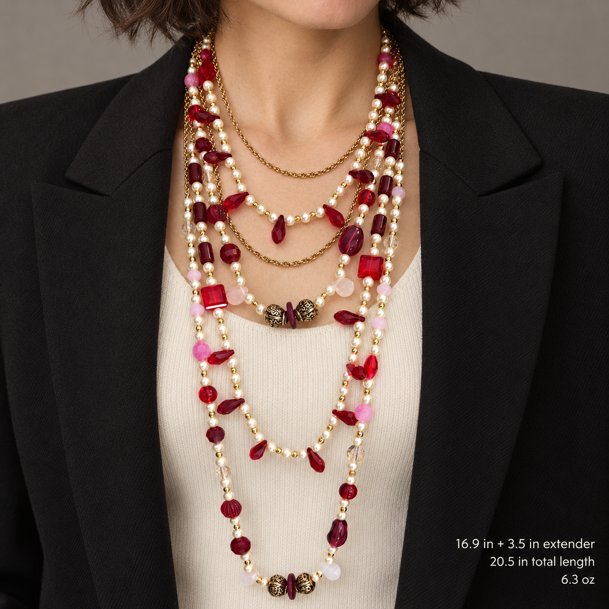 Layered red crystal and pearl-style necklace worn over a cream top with a black jacket