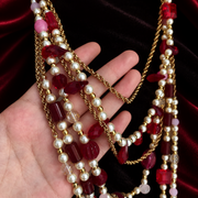 Close-up of red faceted beads, pearl-style beads and gold-tone chains