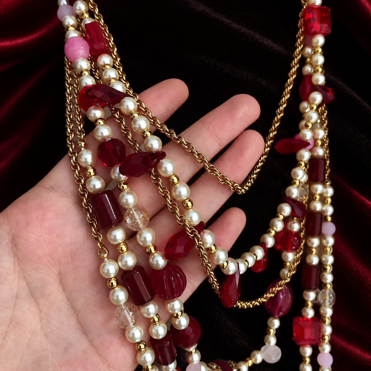 Close-up of red faceted beads, pearl-style beads and gold-tone chains