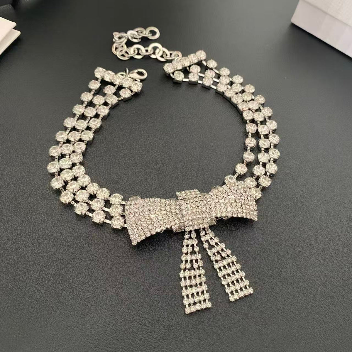 Silver-tone bow choker necklace with three rows of clear faceted stones and dangling bow tails, front view