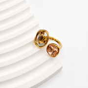 Front view of an open ring with amber and peach faceted glass accents on a white sculptural background