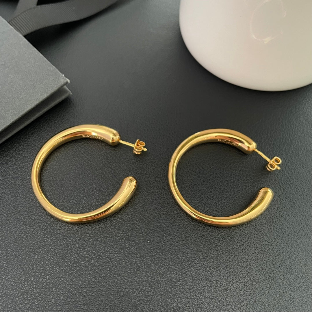 Pair of gold-plated brass hoop earrings on a dark display surface