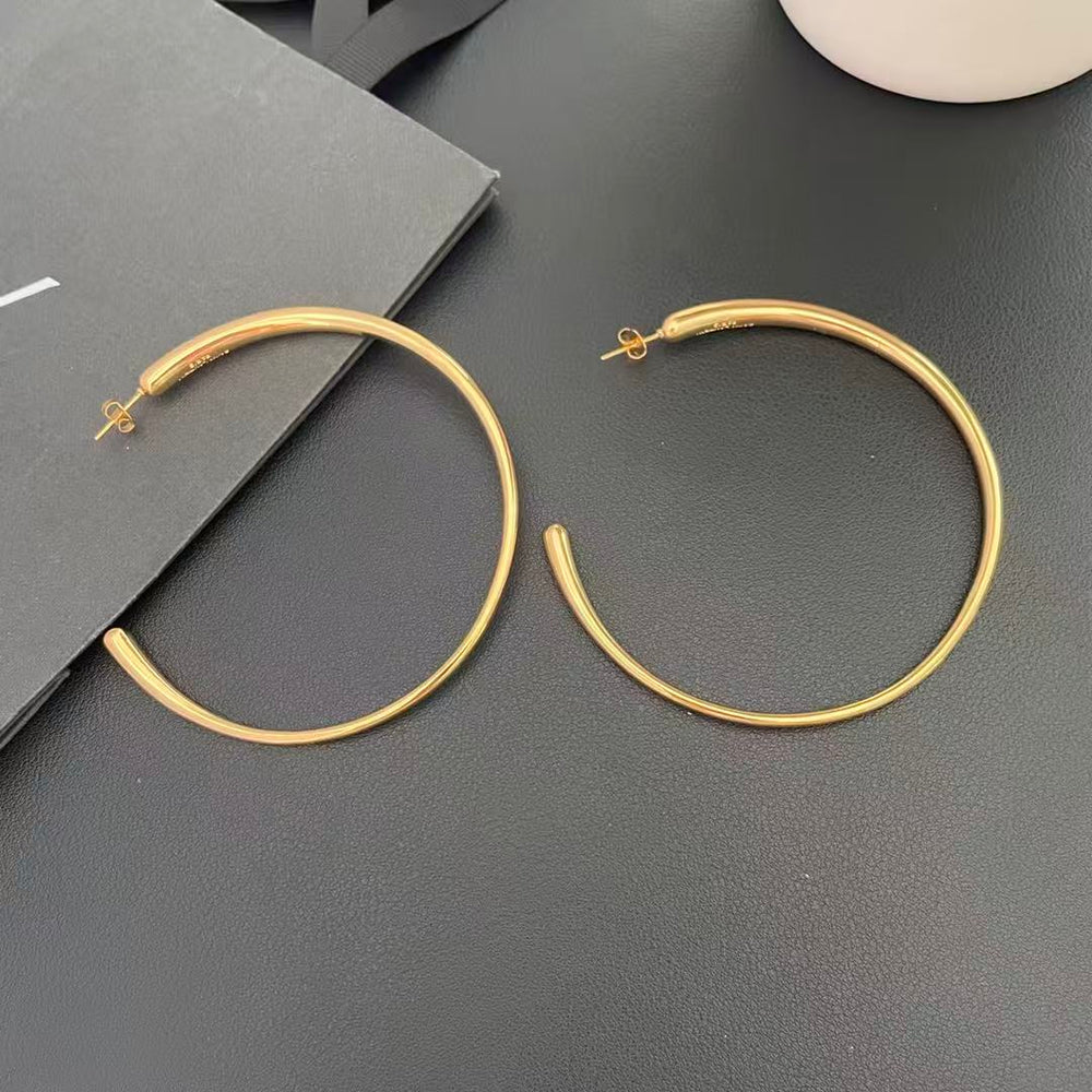 Pair of oversized gold-tone hoop earrings shown on a dark surface