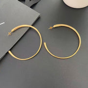 Pair of oversized gold-tone hoop earrings shown on a dark surface