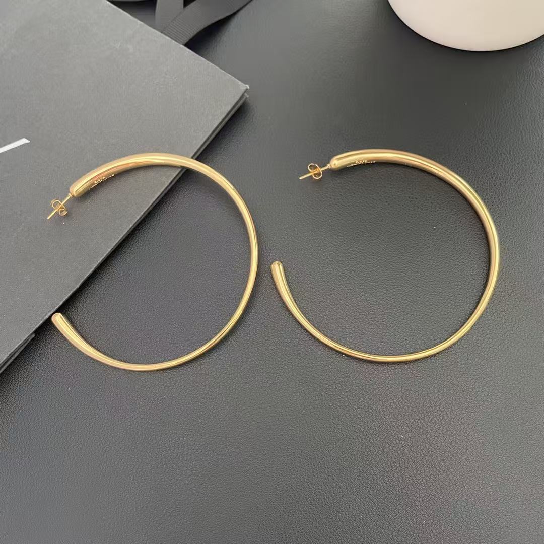 Pair of oversized gold-tone hoop earrings shown on a dark surface