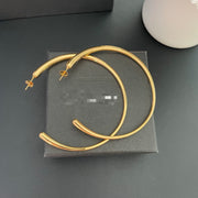 Overlapping pair of oversized gold-tone hoop earrings on a display box