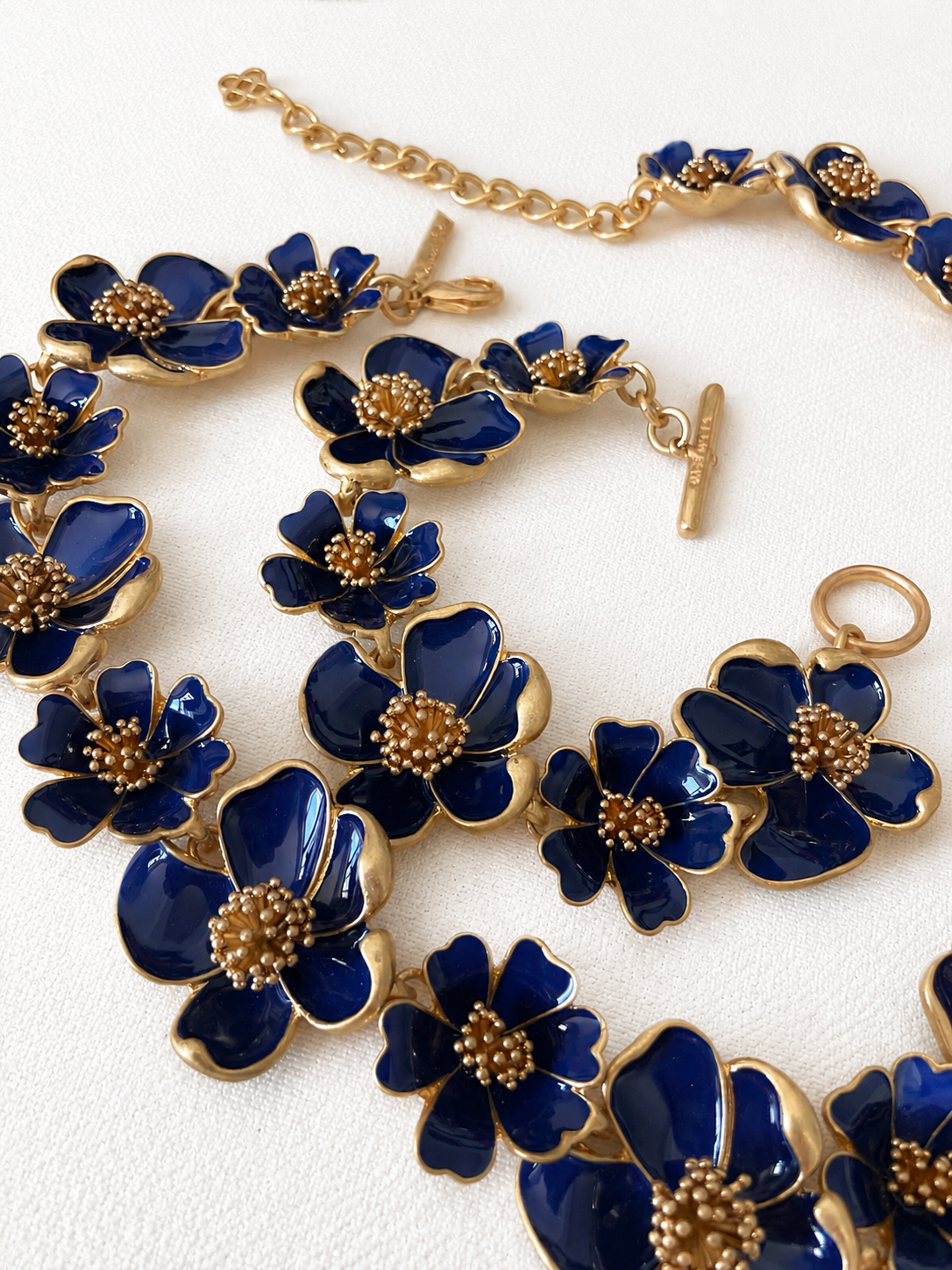 Deep blue enamel floral necklace and bracelet close-up on ivory fabric