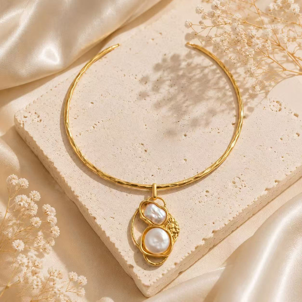 Gold-tone baroque pearl-style pendant choker necklace on neutral stone background