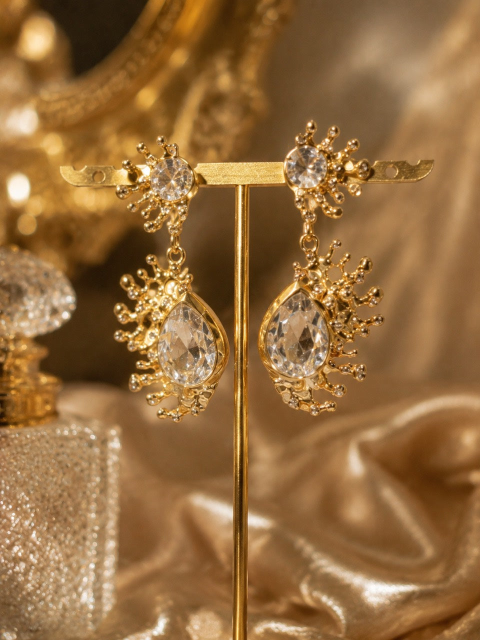 Gold-tone clear rhinestone-style teardrop stud earrings on display stand