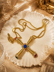 Gold-tone cross pendant necklace with blue red and green cabochon-style accents flatlay