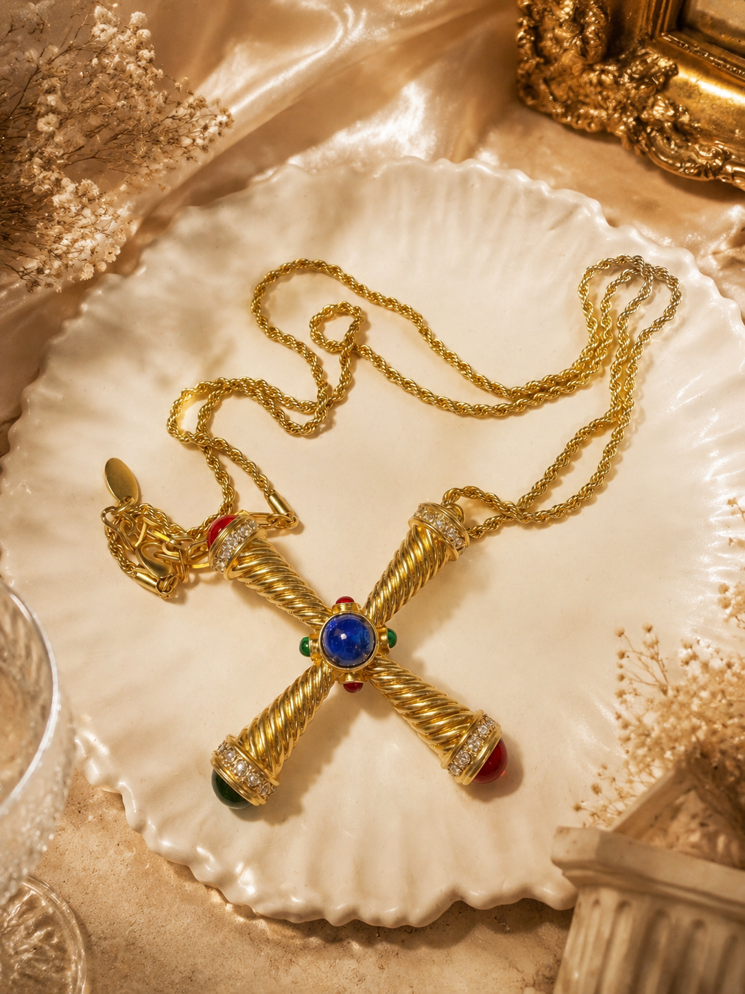 Gold-tone cross pendant necklace with blue red and green cabochon-style accents flatlay