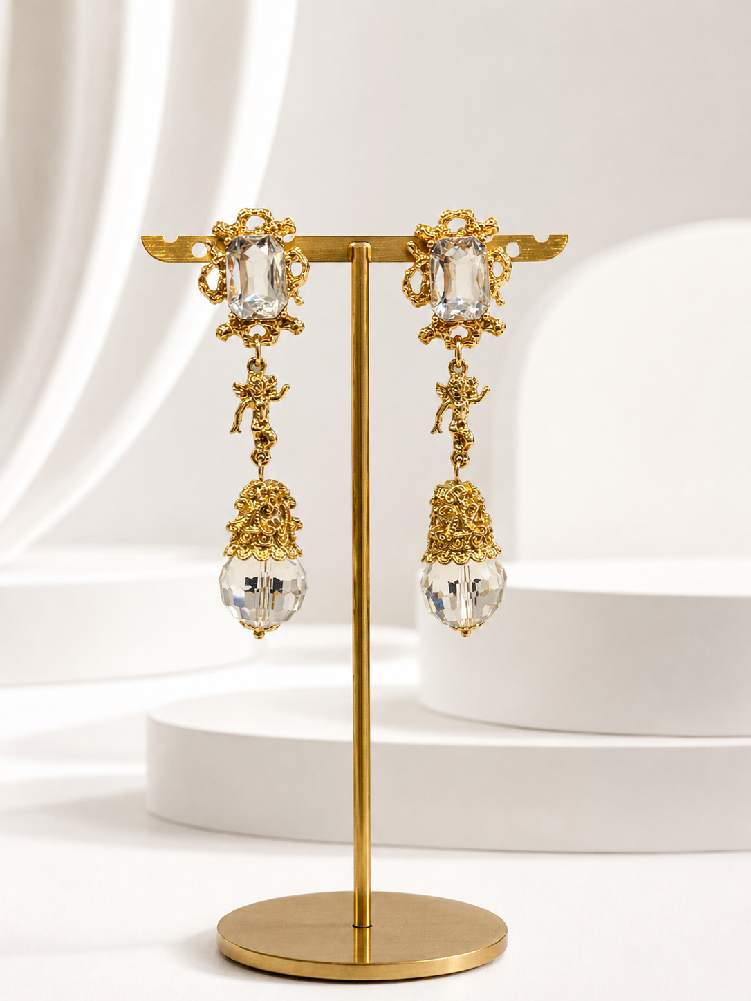 Gold-tone crystal-style glass angel pendant drop stud earrings displayed on a stand