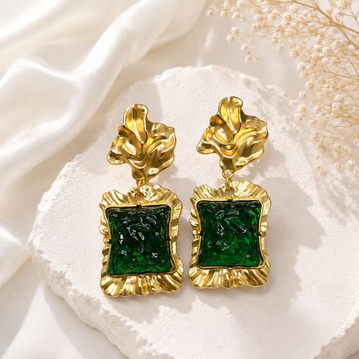 Gold-tone statement stud earrings with sculptural tops and green glass-style square accents