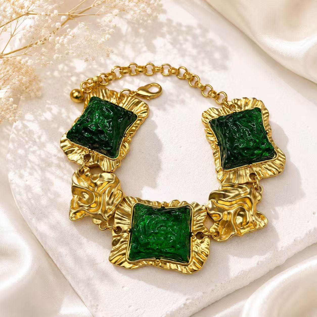 Gold-tone statement bracelet with green glass-style square accents and textured links