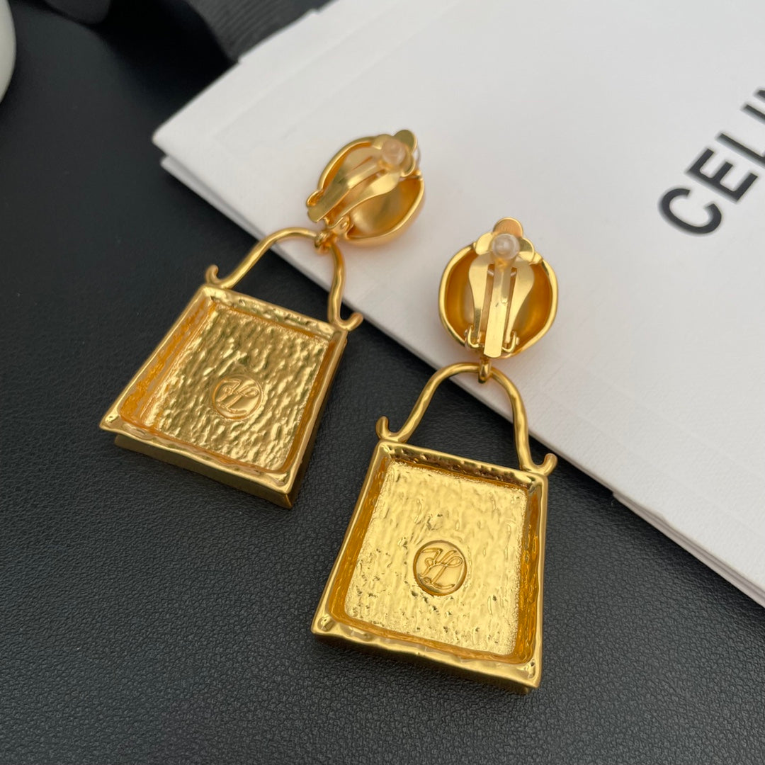 Back view of gold-tone handbag-shaped drop earrings showing clip-on fastenings and clear cushions