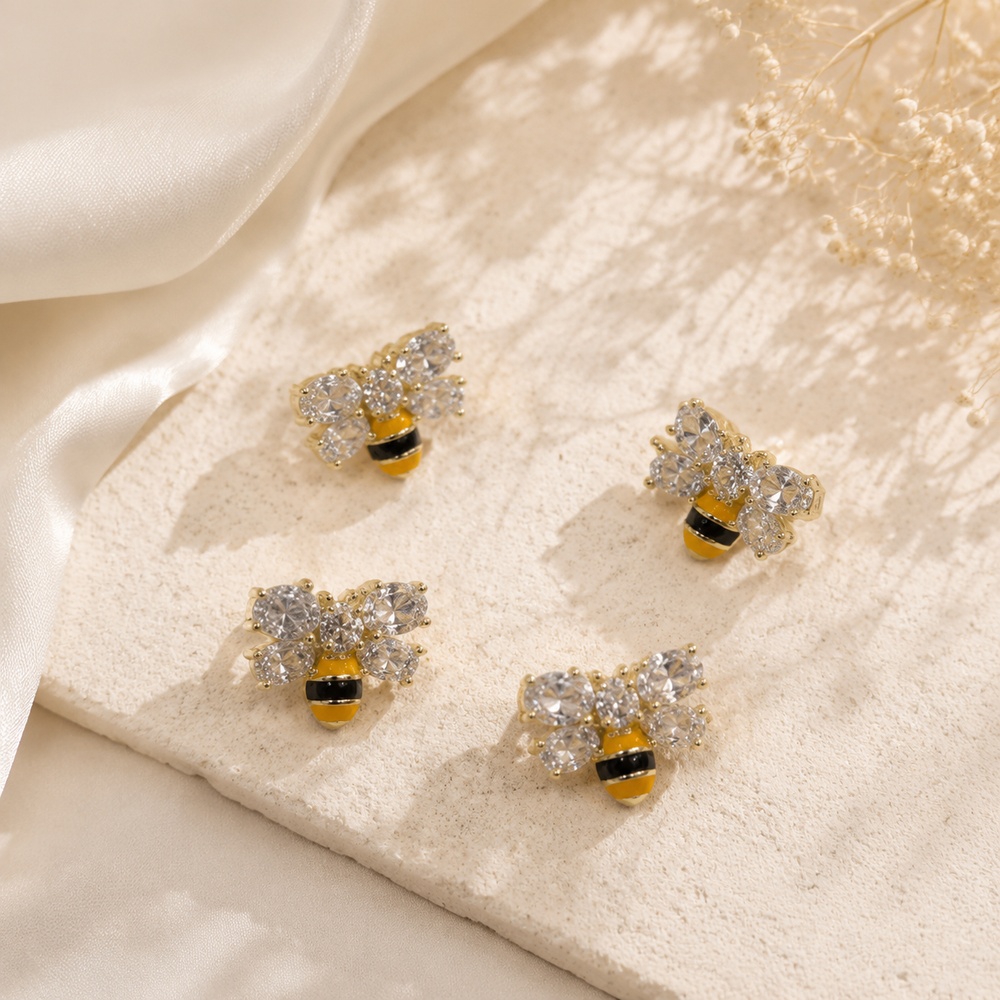 Gold-tone mini bee crystal-style stud earrings with yellow and black stripe details, multiple pairs shown