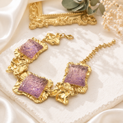 Gold-tone statement bracelet with purple glass-style square accents and textured links