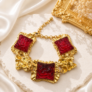 Gold-tone statement bracelet with red glass-style square accents and textured links